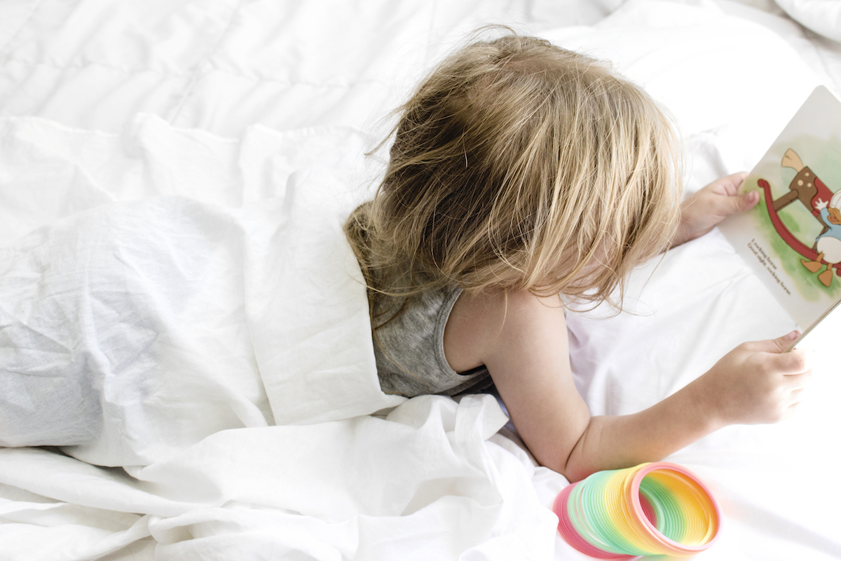 8 tips to create a morning routine for kids - girl reading in bed with a slinky toy.