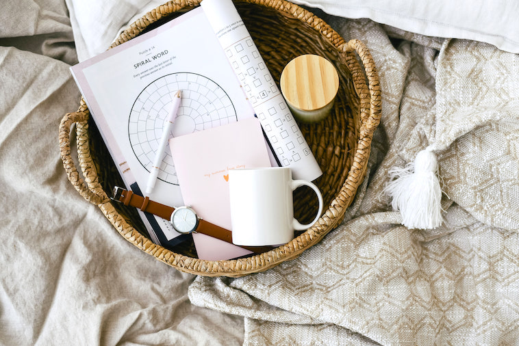 Bed with puzzle book, candle, mug, watch, and pen - a great way to create morning routines for mums.