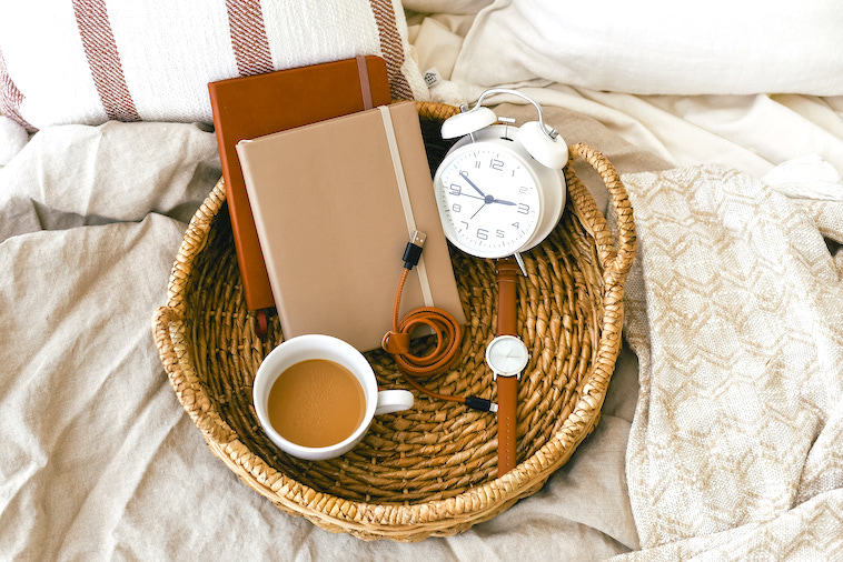 Bed with a basket holding 2 notebooks, a clock, watch and a cup of tea - a great way to create morning routines for mums.