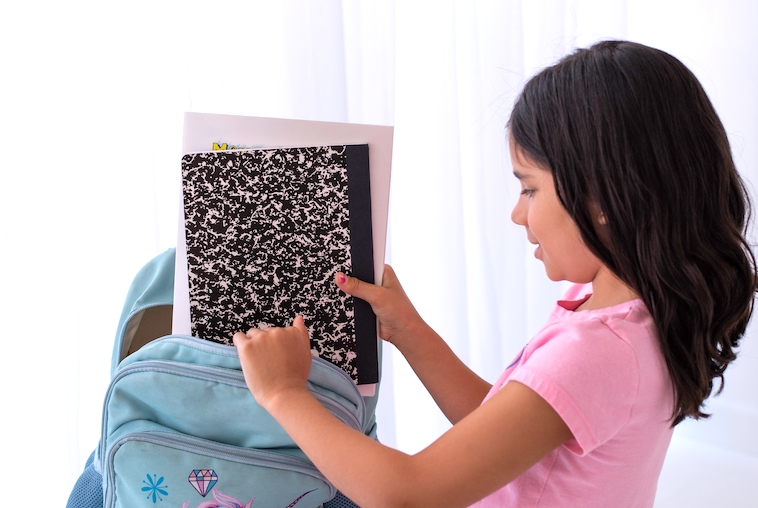 Girl placing a notepad in a back pack - a reason to start thinking about school bag storage ideas