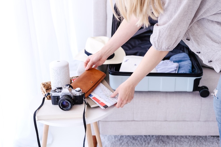 Woman packing a suitcase with clothes, camera and travel documents - one of the ways to plan for a European road trip.