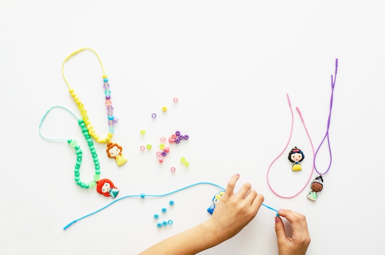 Young child making necklace with beads and doll figures - some of the preschool activities you can try.