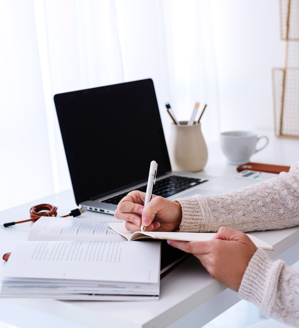 Woman writing a to do list with a laptop nearby - a to do list is a great time management tip.