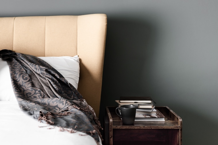 Bed with side table holding magazines and a mug - one way to style your home using interior design tips.