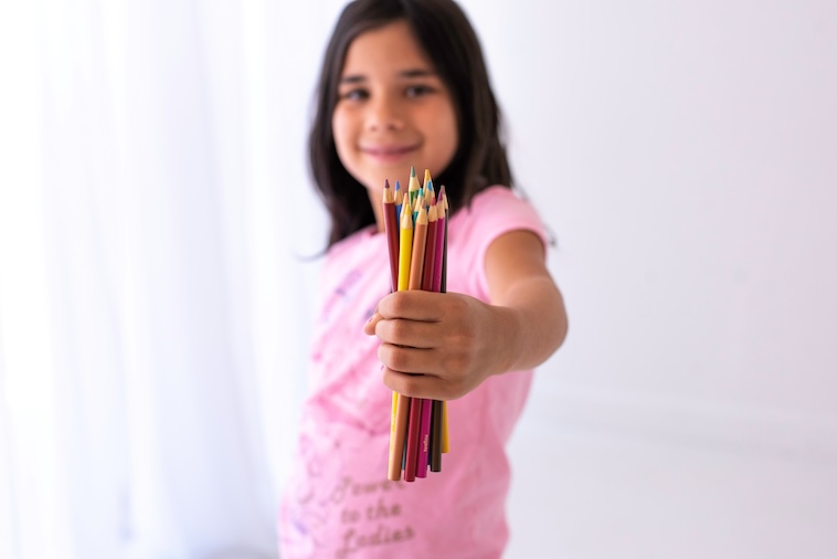 Girl holding colourful pencils - managing school supplies is one of the things you can do to prepare for back to school.