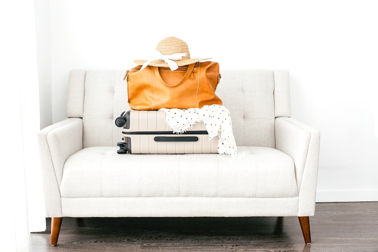 Camel coloured bag, sun hat, scarf, cream suitcase on a grey sofa - tips to make air travel more bearable includes how to pack.