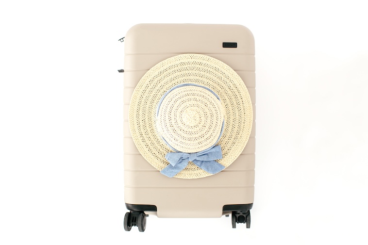 Cream suitcase with sun hat on top - tips to make air travel more bearable includes how to pack.