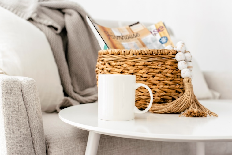 Grey sofa, coffee table with white coffee mug, and wicker basket holding magazines - things you can remove when you want to simplify your home.