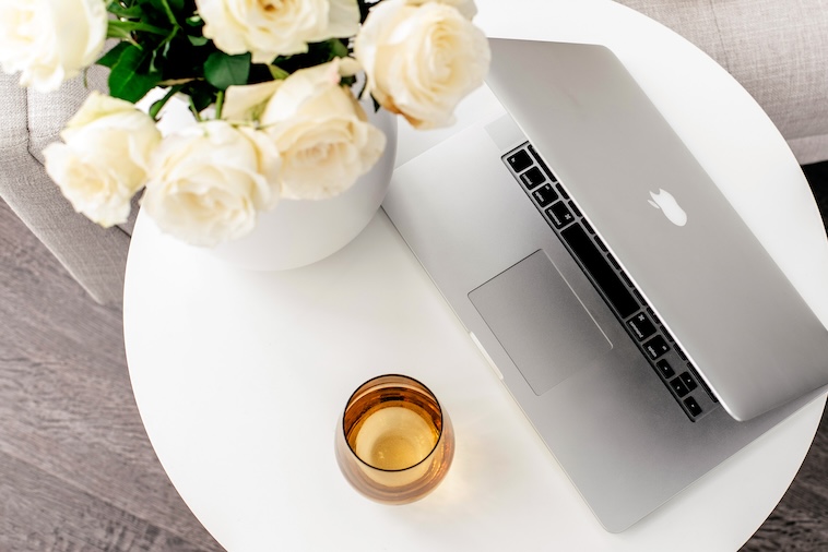 Grey sofa, coffee table with vase and white roses, glass, and open laptop - things you can remove when you want to simplify your home.