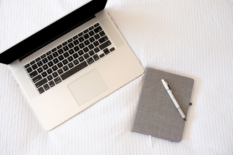 Laptop and notepad on a bed - working from hotels is one of the challenges of working remotely.