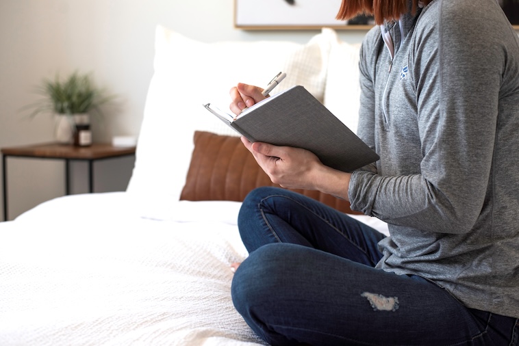 Woman sitting on bed with notepad - working from hotels is one of the challenges of working remotely.