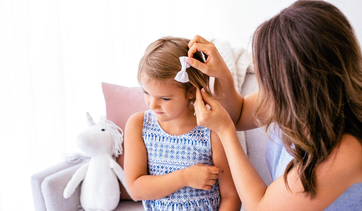 5 tips to make your child's clothes last longer - mother putting a bow in girl's hair.