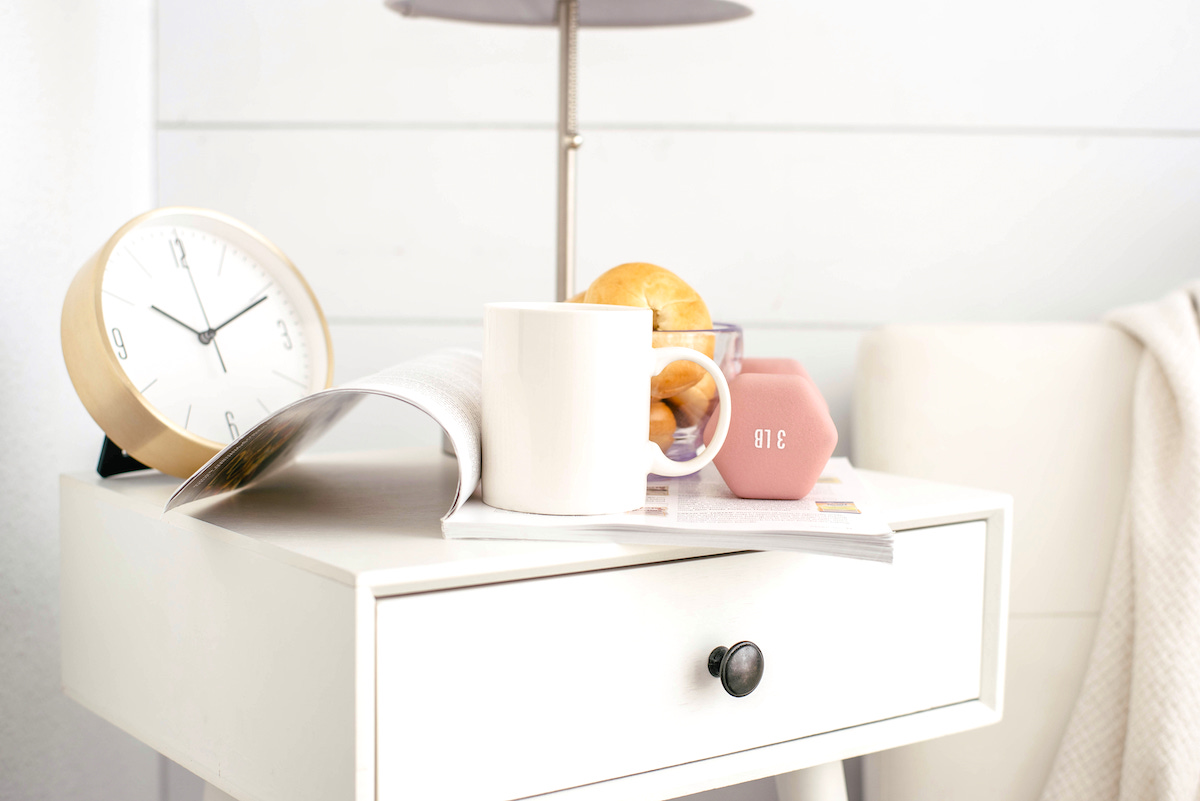 Self-care tips for mums - bedside table with clock, weights, bagels, book and mug
