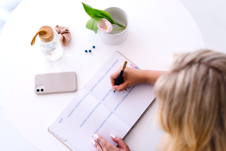 woman writing in a calendar with a phone, tulip, and water bottle - one of the things you can do in 20 minutes.