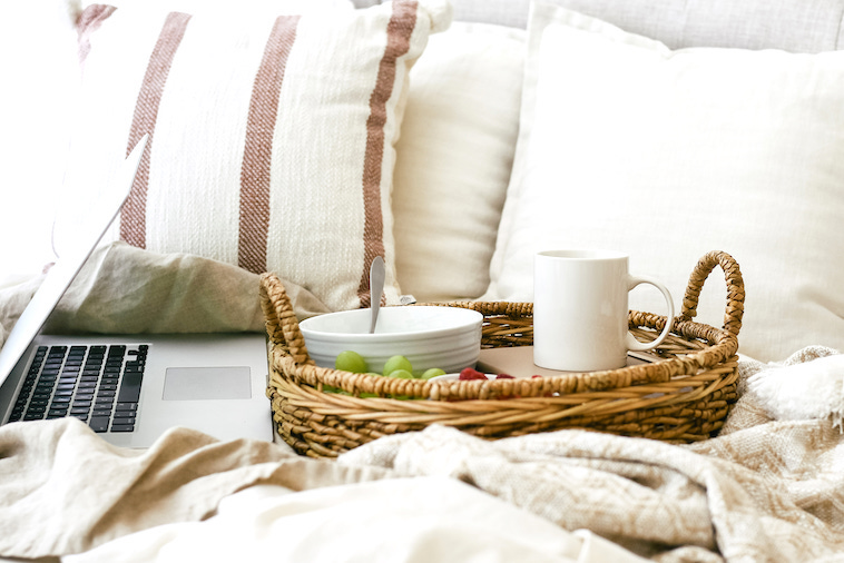 Bed with a laptop, cereal, mug, and fruit - a great way to create morning routines for mums.