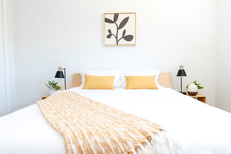 Bedroom with bed, 2 yellow cushions, floral print, 2 bedside tables, 2 lamps - updating bedrooms is one of the home improvement ideas you can try.