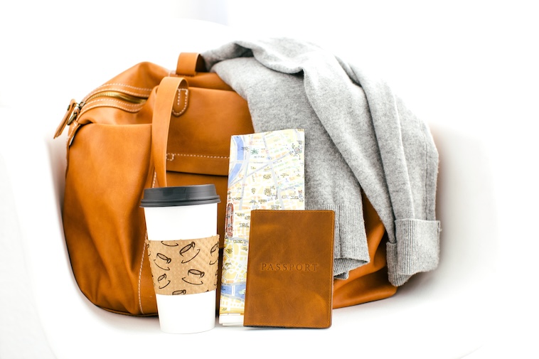 Camel coloured bag with jumper, passport, coffee cup and map - tips to make air travel more bearable includes how to pack.