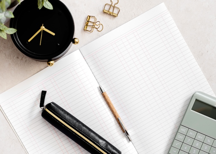 Black clock, paper clips, pen, calculator, and notebook - things you need when managing money as a busy mum.