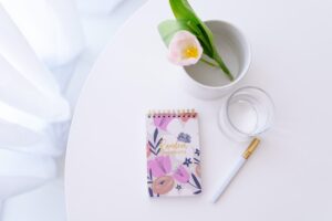 Table with notepad, pen, glass of water, pink flower - things you need when writing goal ideas.